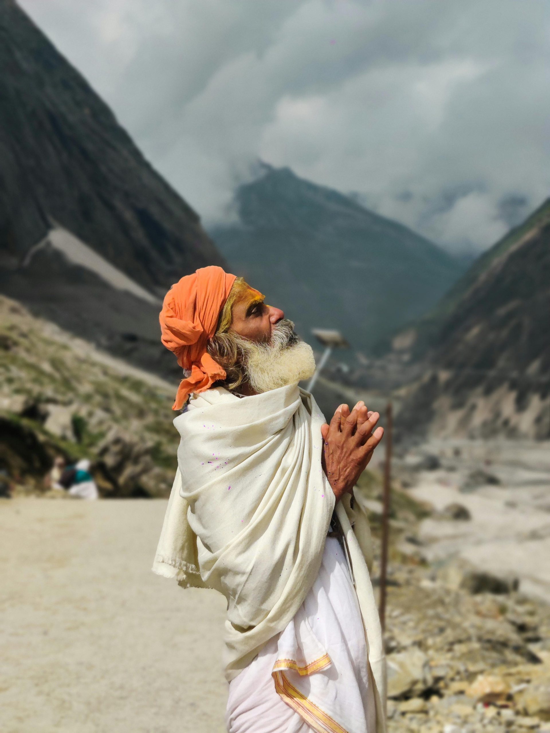 A senior man in traditional attire prays amidst the majestic Himalayan landscape in Jammu, India.