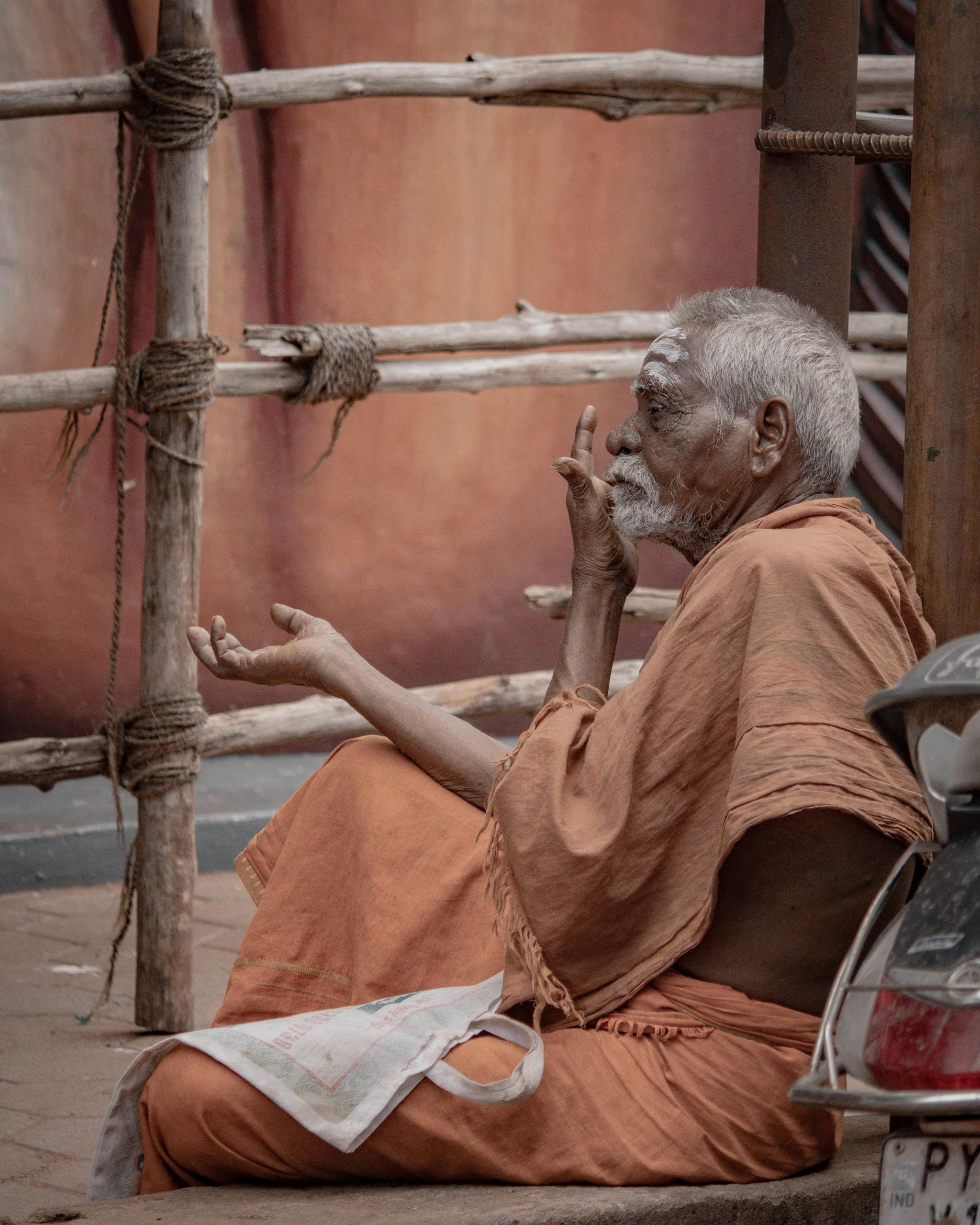 Senior Hindu monk in traditional attire meditating outdoors in Puducherry, India.