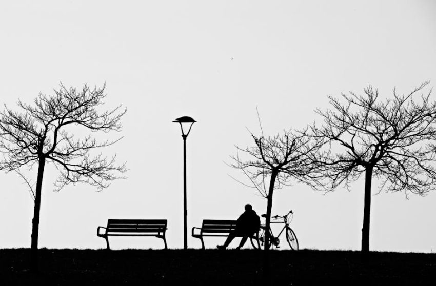 A figure sits still on a bench, not waiting for anything in particular—just being.