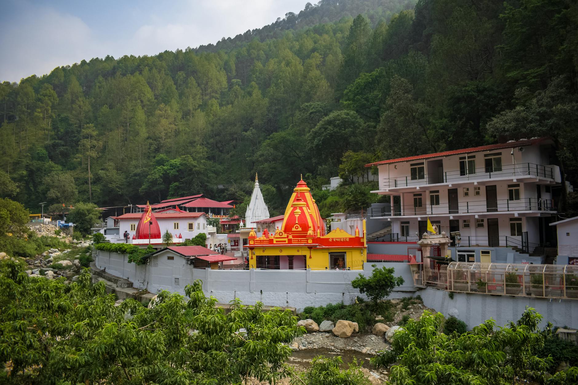 Hindu temple complex surrounded by lush forested hills, showcasing vibrant architecture and serene nature.