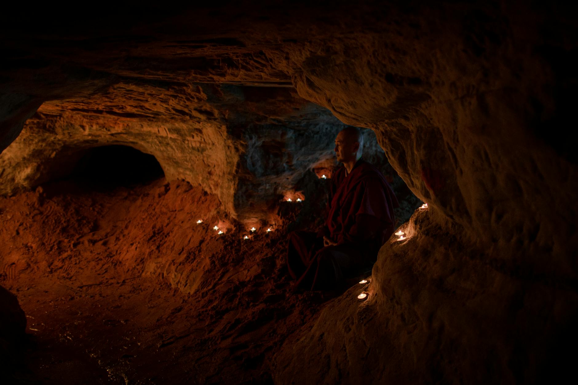 A Buddhist monk meditates in a candlelit cave, showcasing spirituality and serenity.