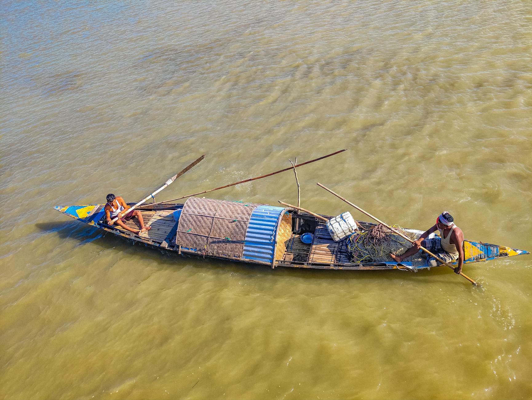 Fishermen navigate a wooden boat on the Brahmaputra River in Assam, India.