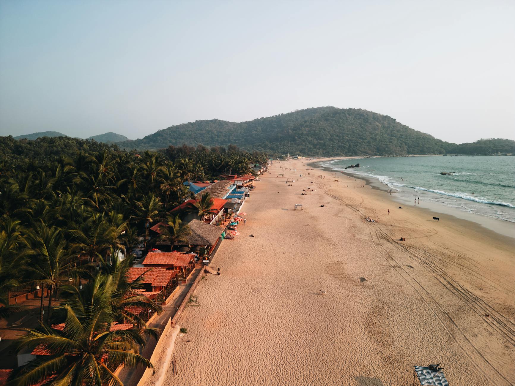 Scenic aerial view of Palolem Beach, Goa during sunset, showcasing sandy shores and lush green surroundings.