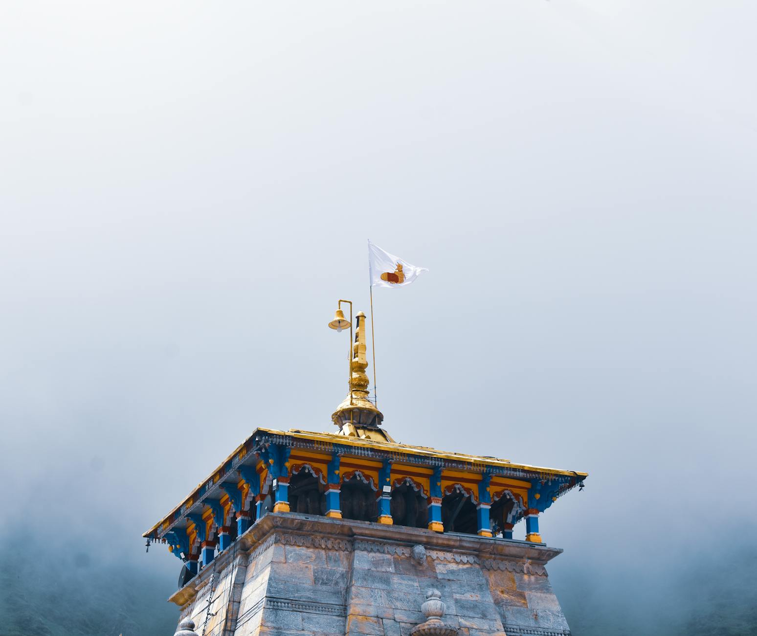 A striking temple tower with a golden spire and flag amidst a misty background, showcasing traditional architecture.