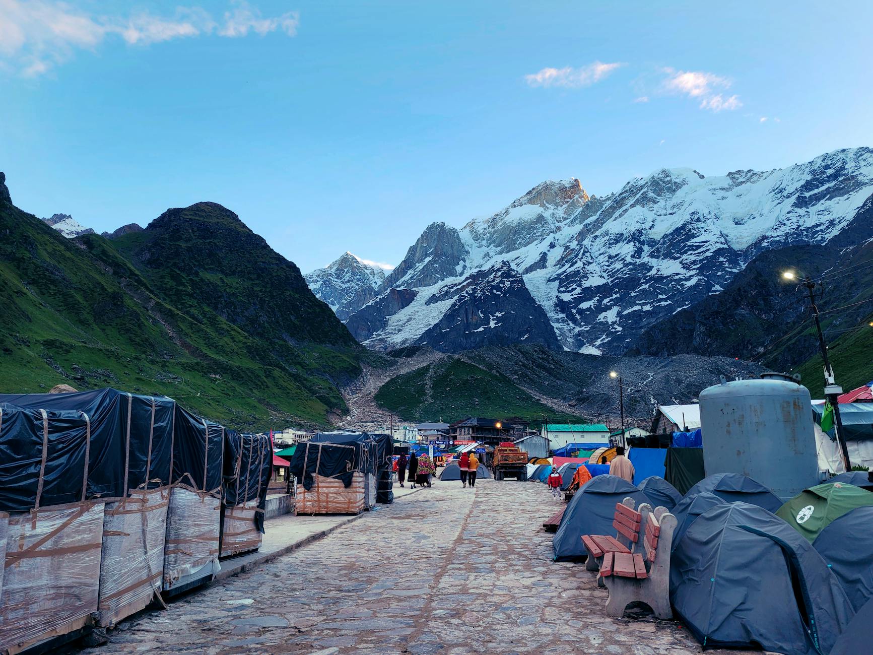 Picturesque Kedarnath setting with majestic snow-covered mountains and tents along a pathway.