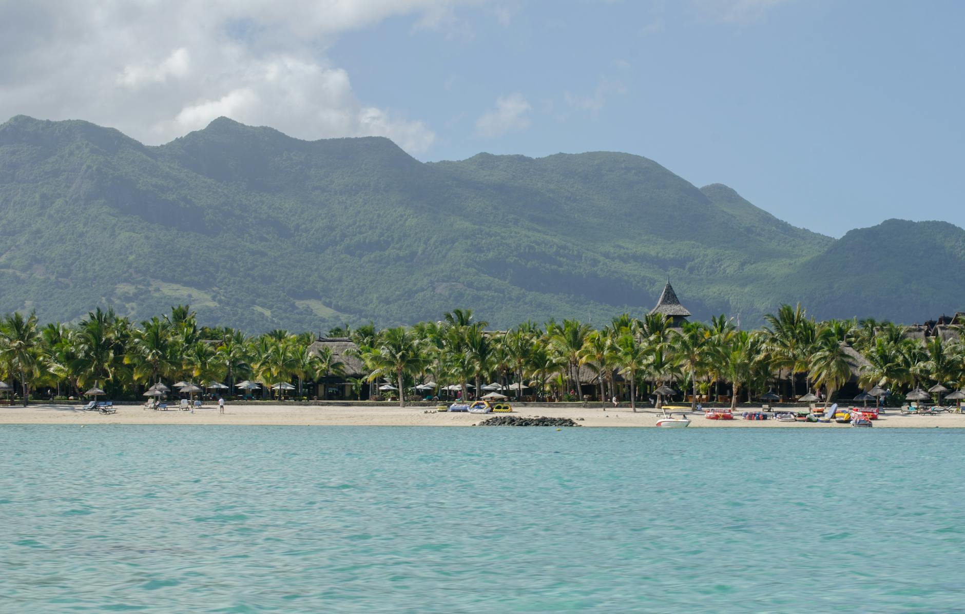 Peaceful tropical beach scene with palm trees, azure sea, and distant mountains.