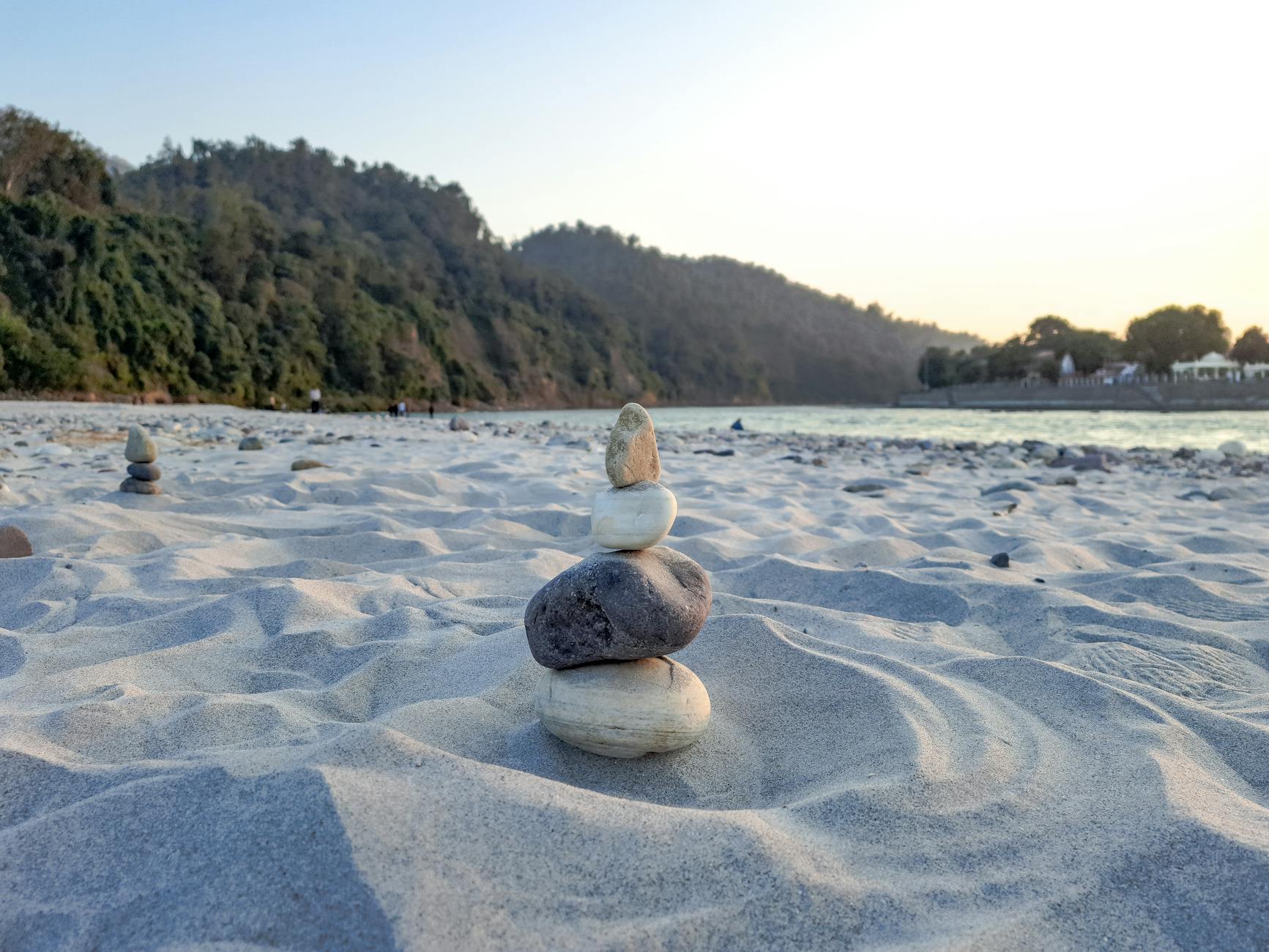 A serene view of stacked stones on a sandy Ganges riverbank in Rishikesh, India.