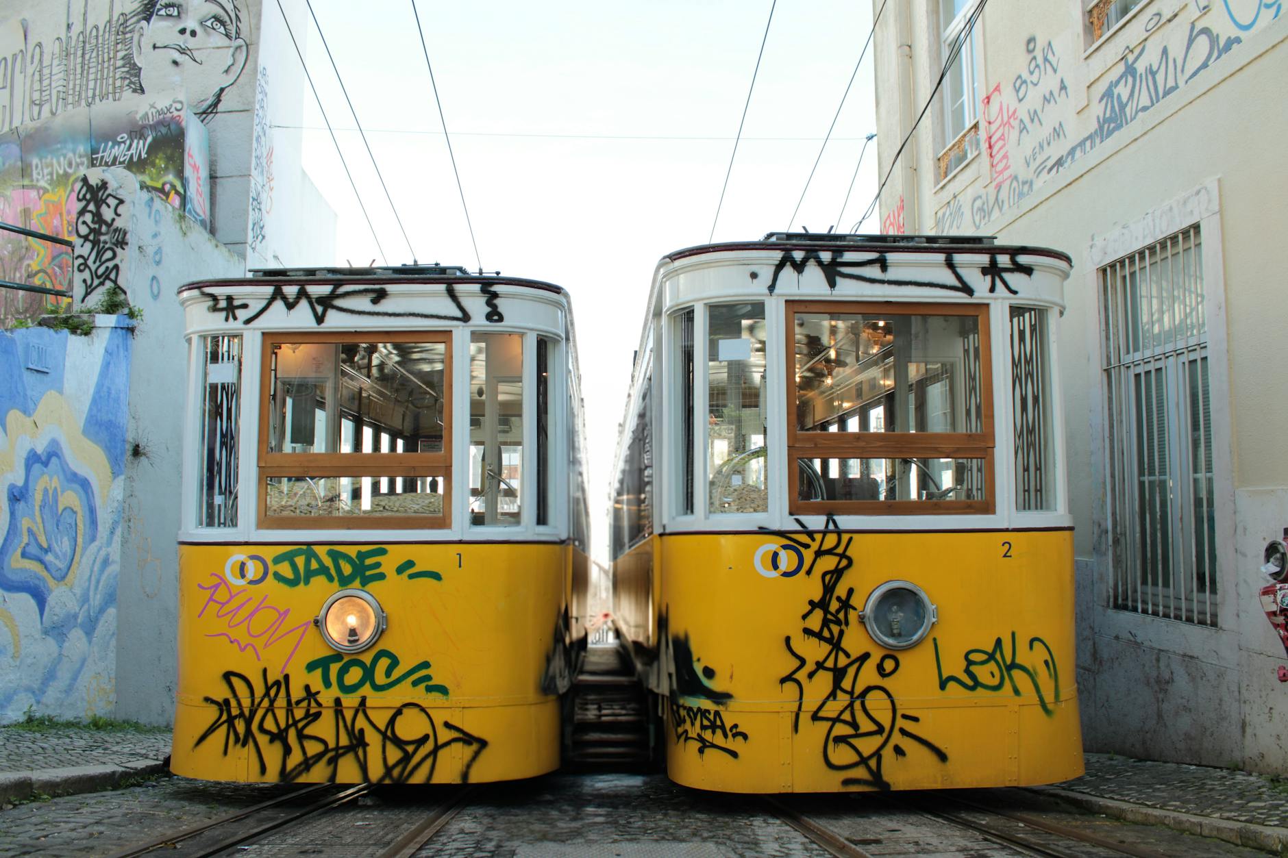 Two iconic yellow trams in a graffiti-covered street in Lisbon, Portugal. Vibrant urban scene.