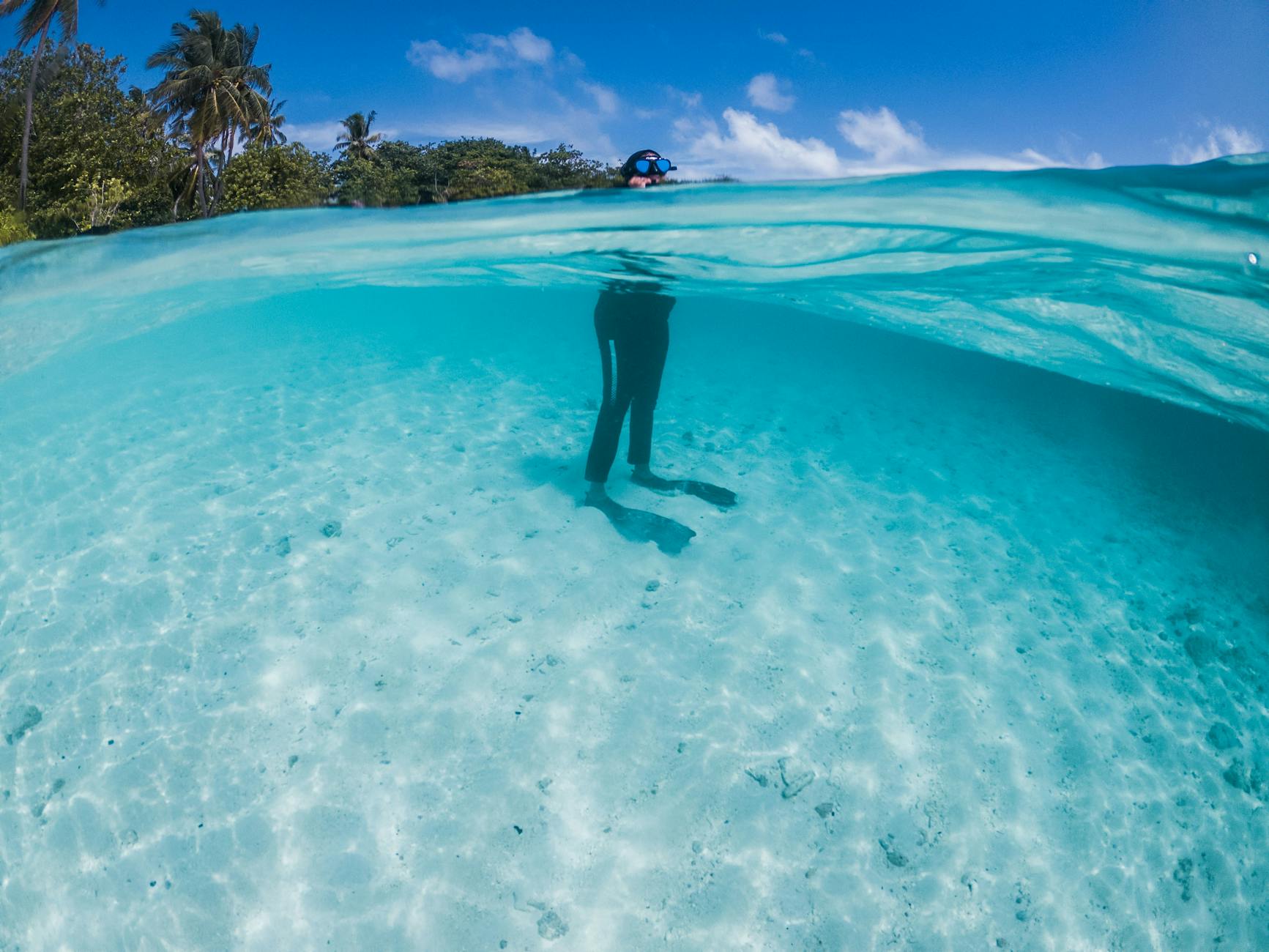 Unrecognizable person in snorkeling mask and goggles standing in transparent blue seawater in tropical nature on sunny clear day