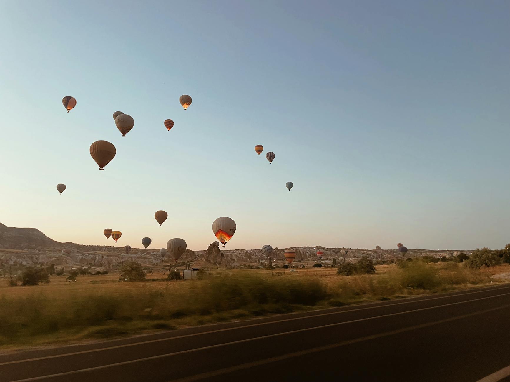 Scenic view of hot air balloons floating over the Cappadocia landscape at sunrise in Türkiye.
