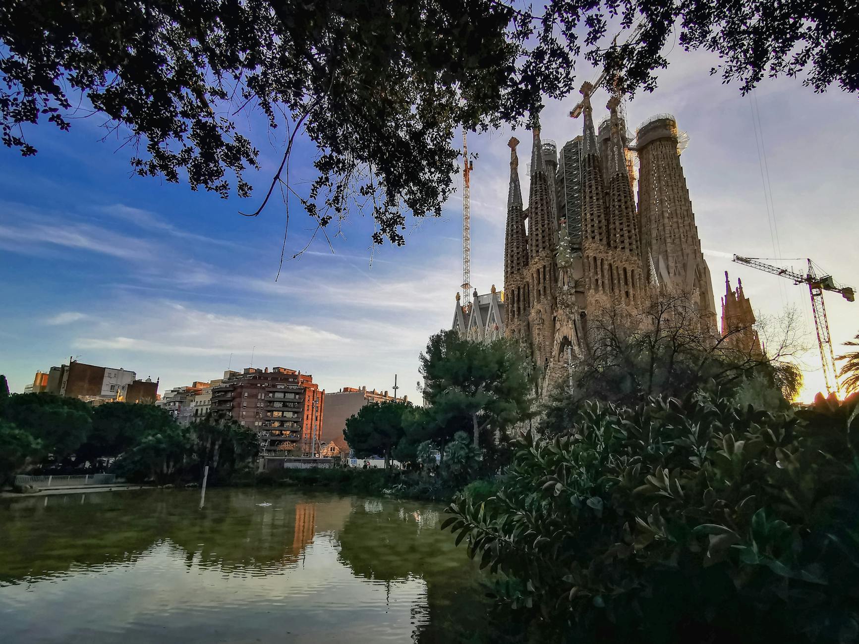 Capture of the iconic Sagrada Familia in Barcelona at sunset with reflections on a nearby pond.