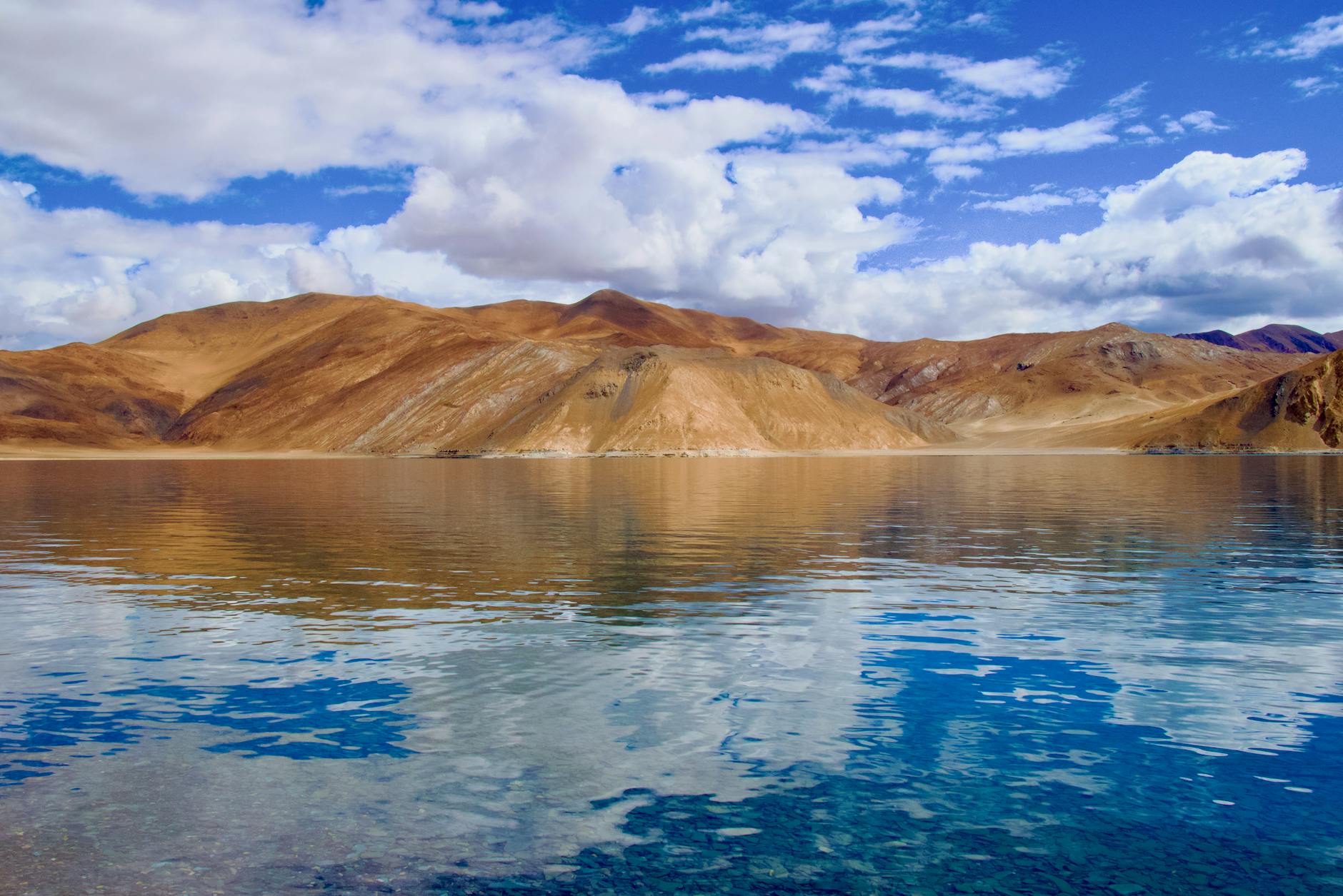 Stunning view of Pangong Tso Lake reflecting arid hills and blue sky. Perfect for travel inspiration.