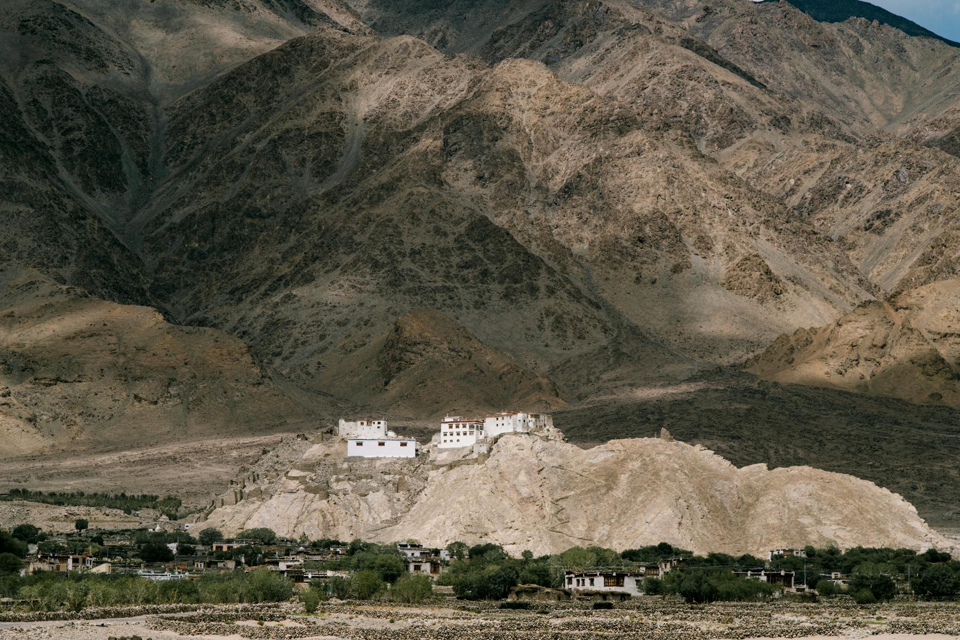 Little settlement located on grassy ground in mountainous area near rock with buildings on top in nature in rural terrain