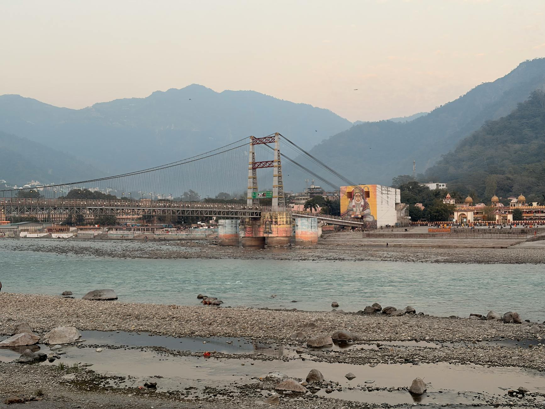 Laxman Jhula bridge spanning Ganges River in Rishikesh with mountainous backdrop.