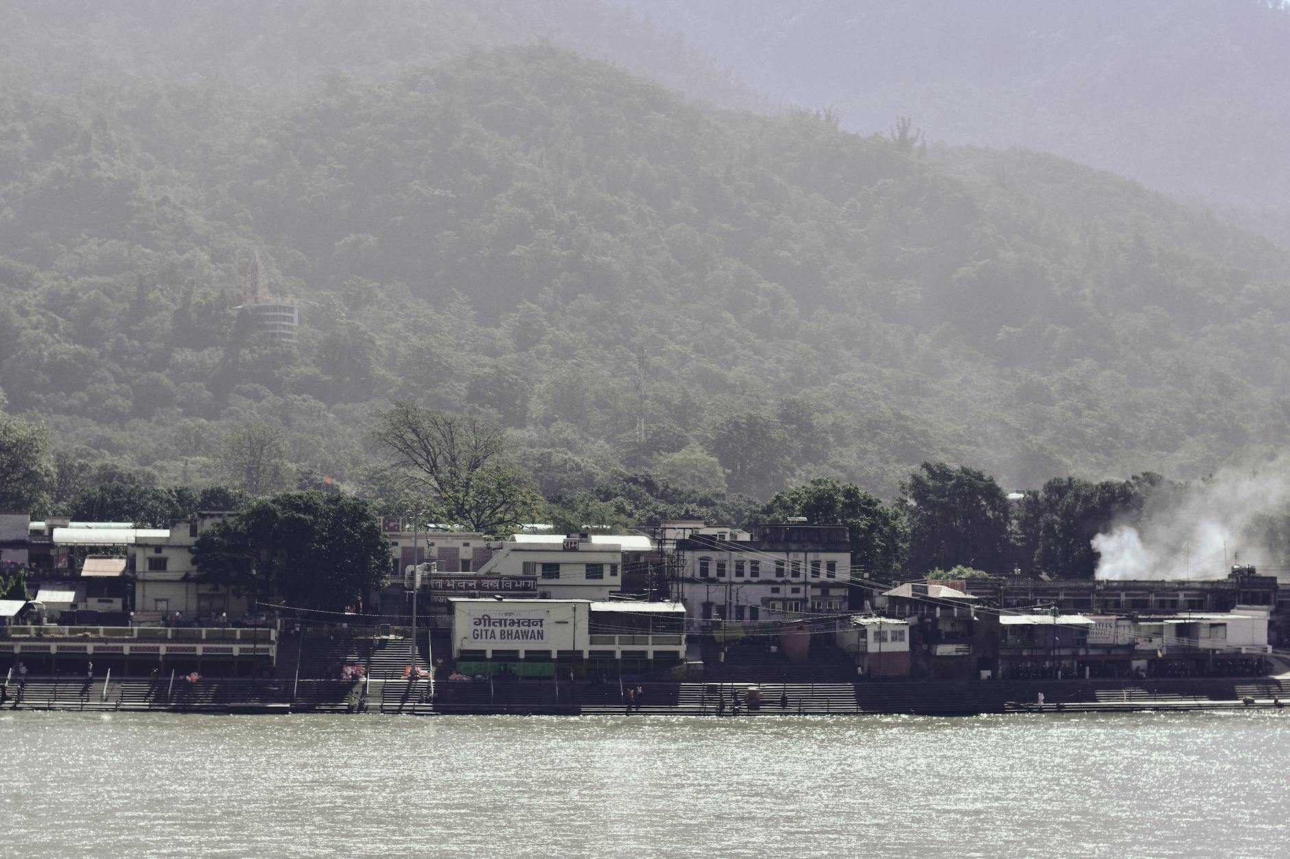 View of a tranquil riverside village with dense green hills in the background, ideal for travel and nature scenes.
