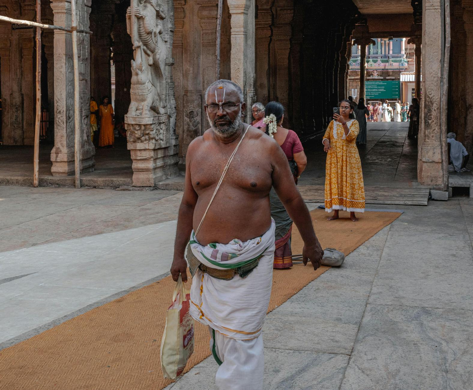 A man in traditional attire walking through an ancient temple in Tamil Nadu, India.