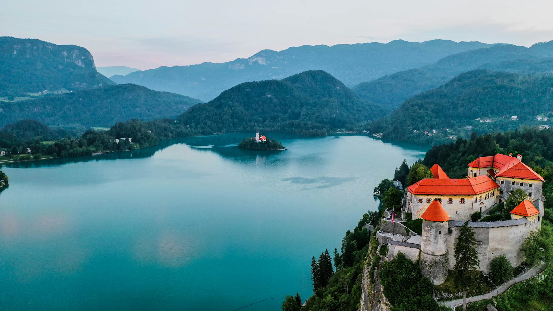Breathtaking aerial view of Bled Castle overlooking Lake Bled in Slovenia surrounded by mountains.