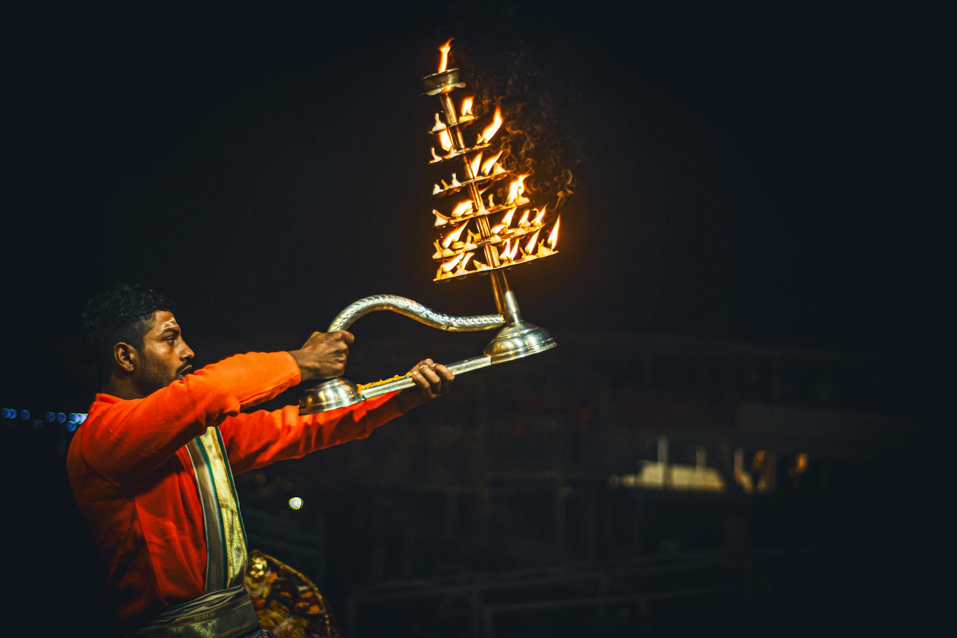 A man performs a Hindu ritual with a lit Aarti lamp during a night ceremony at Varanasi Ghats.