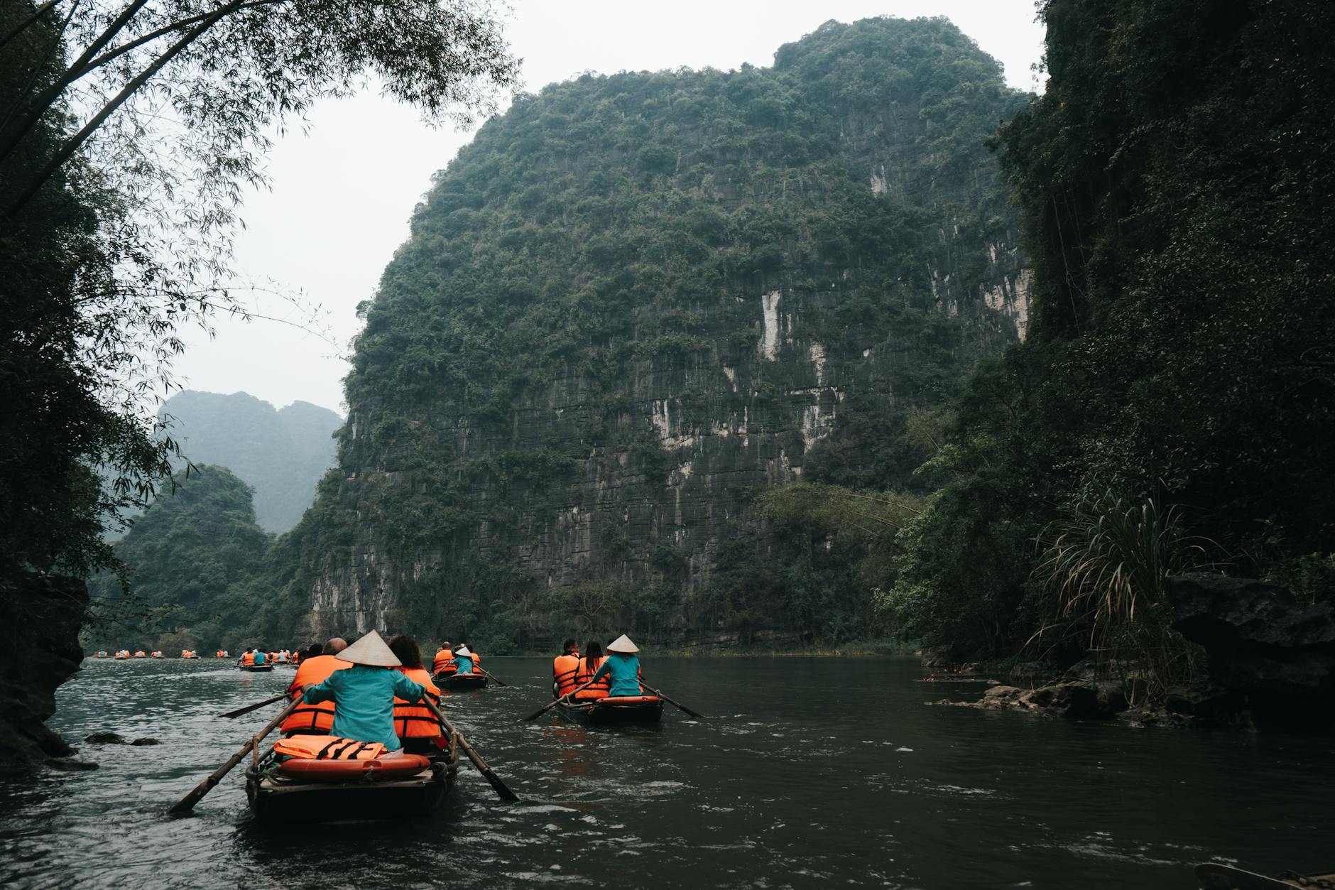 Tourists paddle down a river in Ninh Binh, Vietnam, surrounded by majestic limestone cliffs.